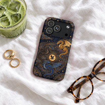 A dark blue phone case with a golden dragon design rests on white fabric next to glasses, rings, and iced matcha.