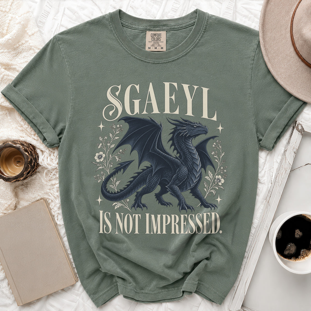 Sage green t-shirt with a black dragon and floral design; text reads "SGAEYL IS NOT IMPRESSED."
