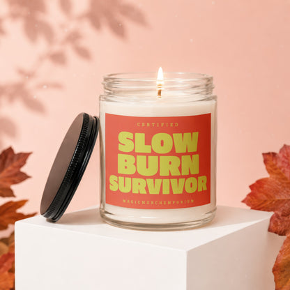 Burning candle in a glass jar with a red label that says "CERTIFIED SLOW BURN SURVIVOR".