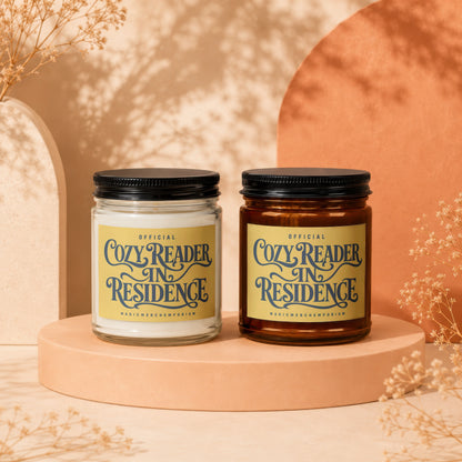 Two candles with "Cozy Reader In Residence" labels on a display stand.