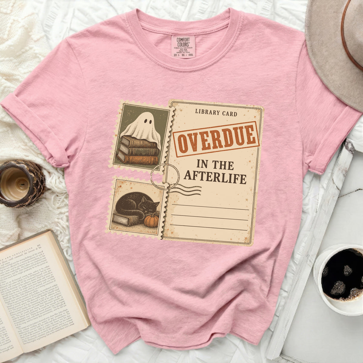 Pink t-shirt with graphic of ghost on books and library card "Overdue in the Afterlife".
