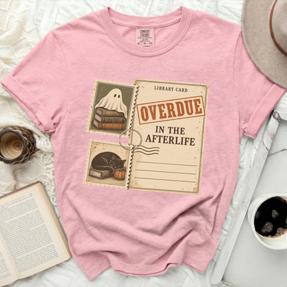 Pink t-shirt with graphic of ghost on books and library card "Overdue in the Afterlife".
