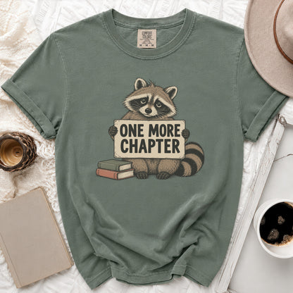 Green t-shirt with a raccoon holding a sign that says "ONE MORE CHAPTER".