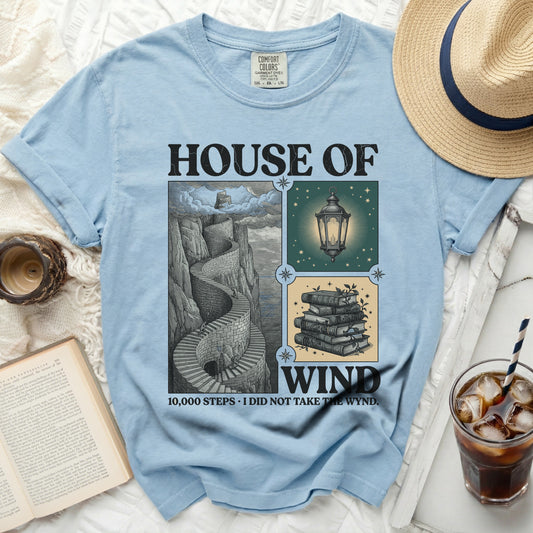 Light blue t-shirt with "House of Wind" and staircase, lantern, and book illustrations.