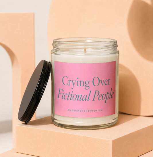 Candle with pink label reading "Crying Over Fictional People" and "MAGICMERCHEMPORIUM".