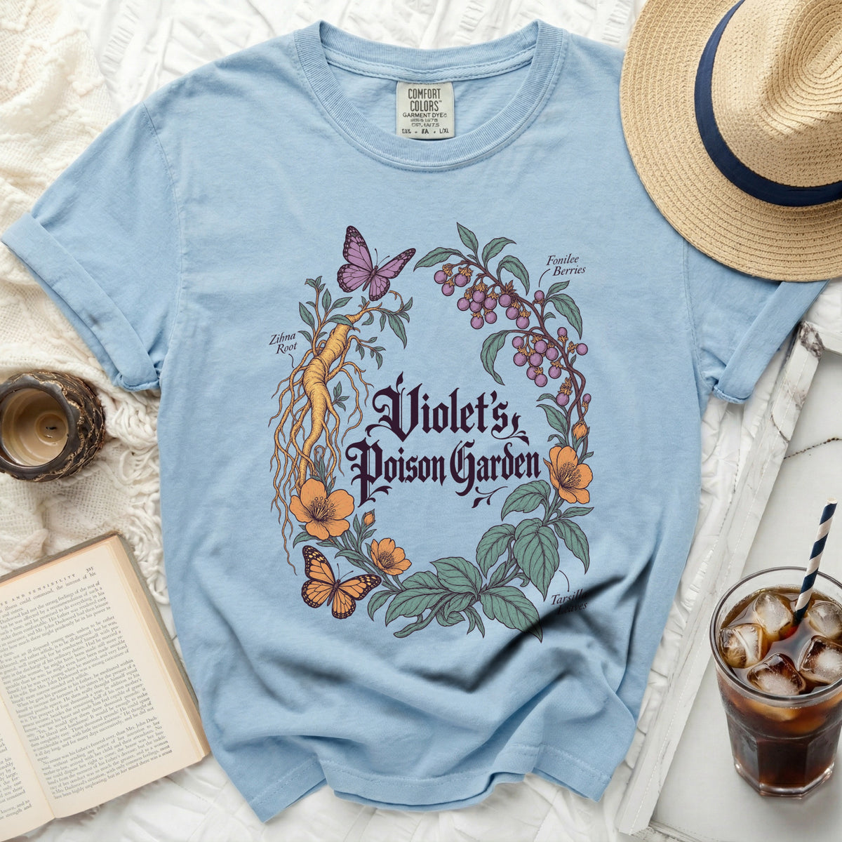 A light blue t-shirt featuring a botanical illustration with the text Violet's Poison Garden.