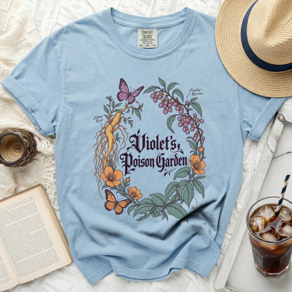 A light blue t-shirt featuring a botanical illustration with the text Violet's Poison Garden.
