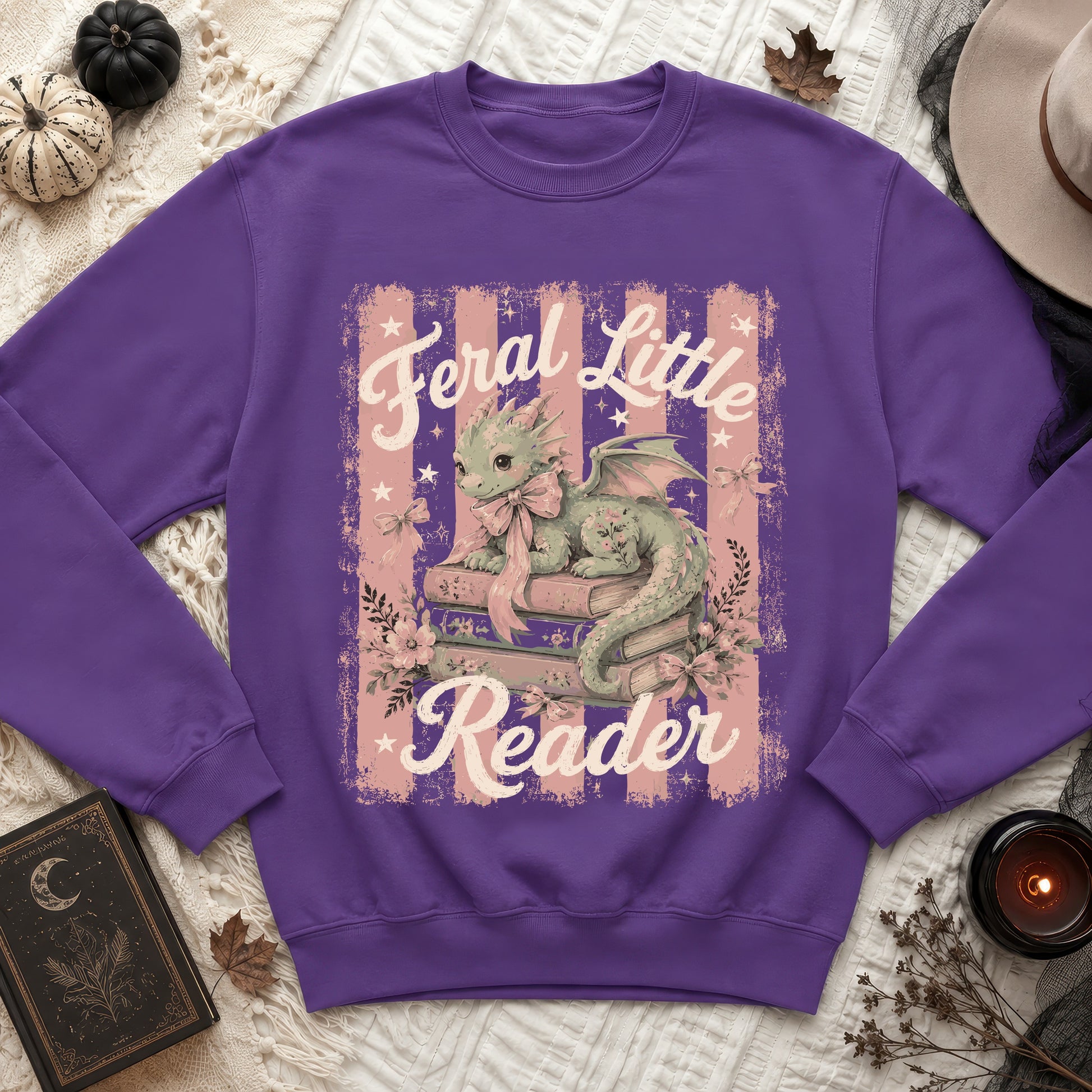 Purple sweatshirt with a cute dragon and books graphic that says "Feral Little Reader".