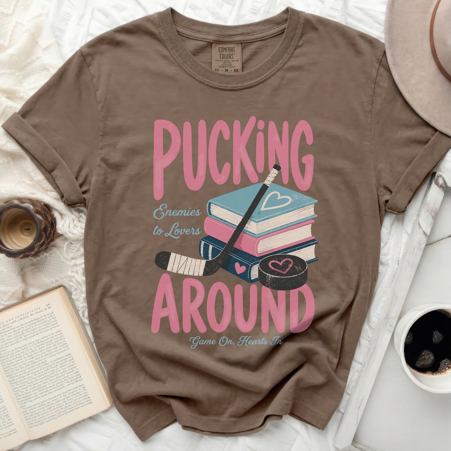 Brown t-shirt with "Pucking Around Enemies to Lovers" graphic and books.