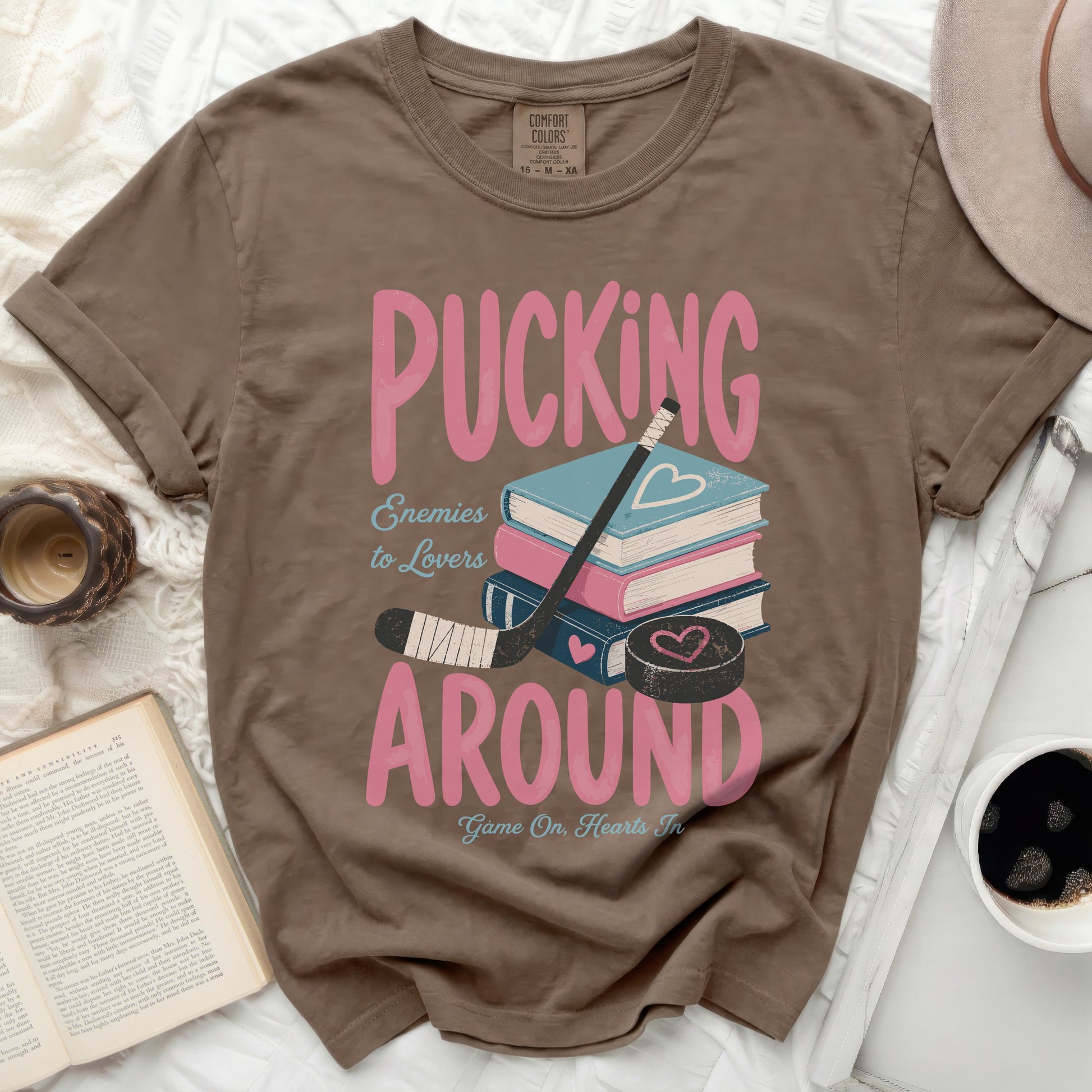 Brown t-shirt with "Pucking Around Enemies to Lovers" graphic and books.
