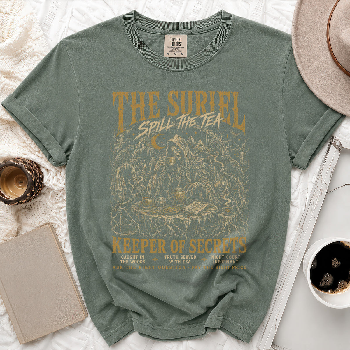 Green t-shirt with "The Suriel Spill The Tea Keeper of Secrets" graphic.