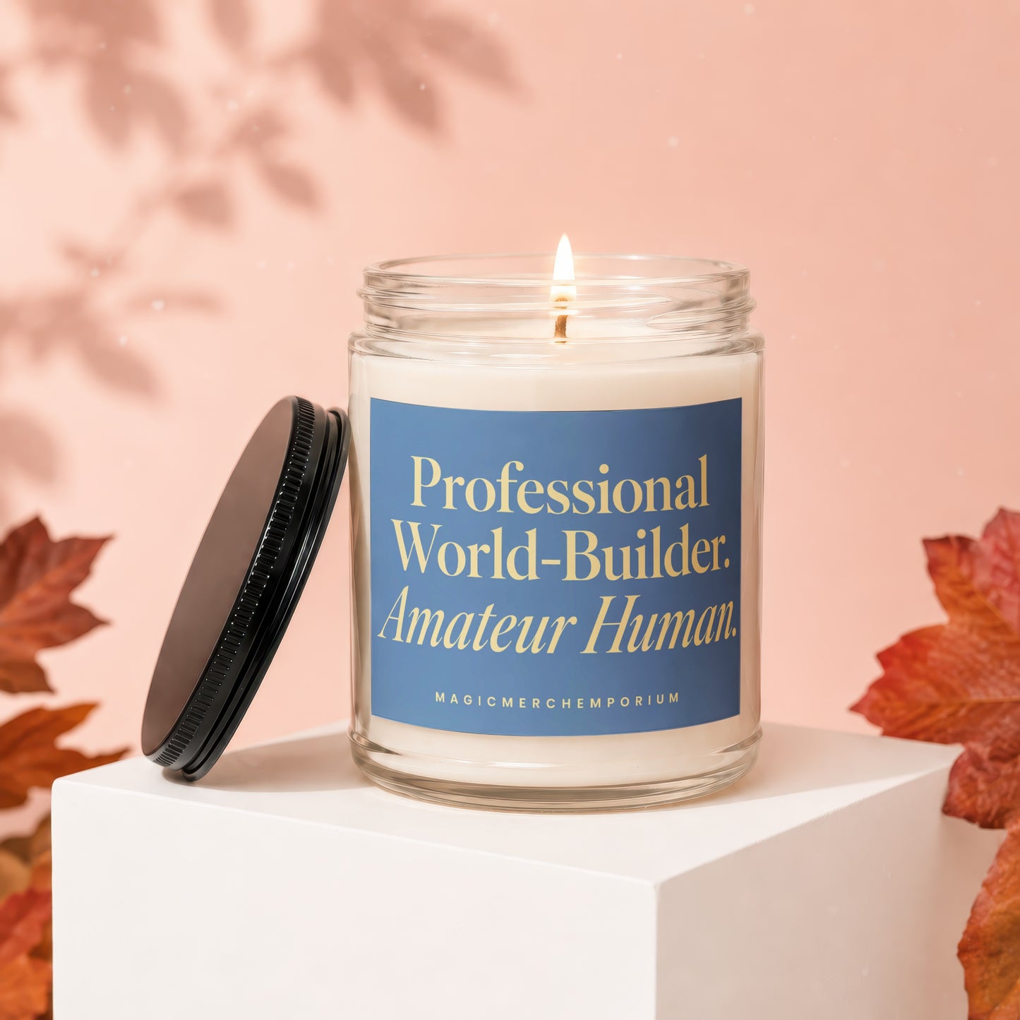 Glass jar candle with blue label reading "Professional World-Builder. Amateur Human."