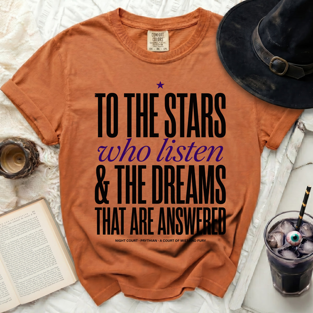 Orange t-shirt with "To the Stars who Listen" text, witch hat, and drink.