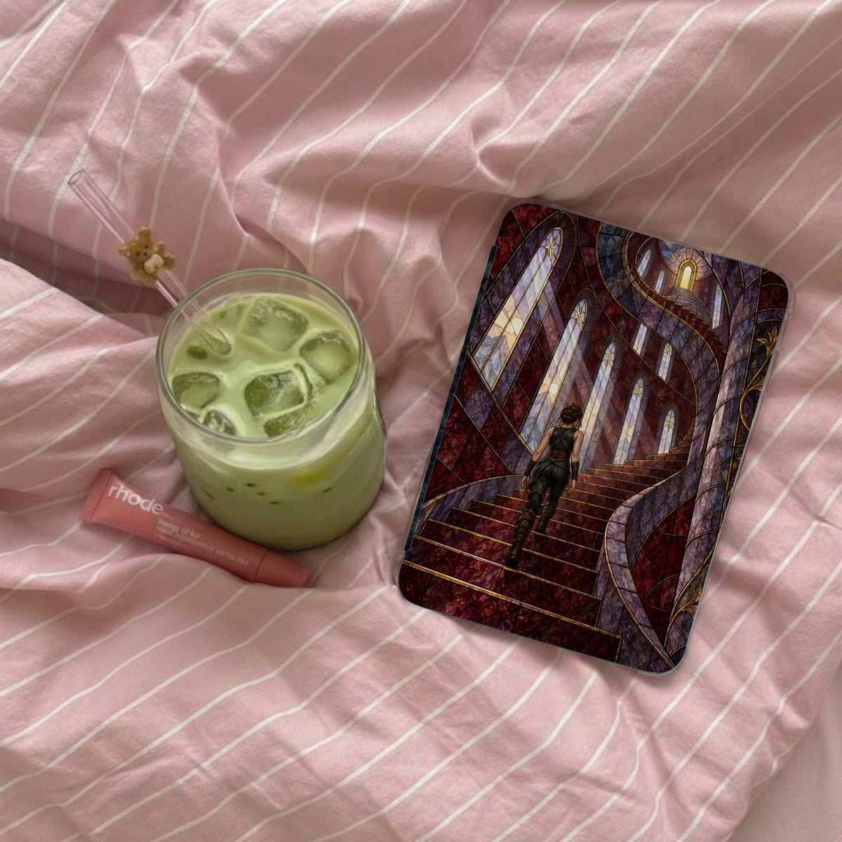 Green drink and makeup tube next to a phone case with a woman on a staircase.
