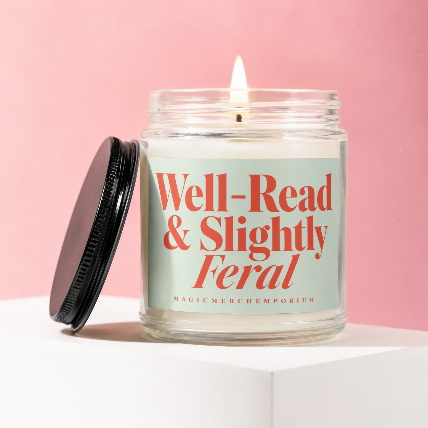 Lit candle in glass jar with black lid, featuring "Well-Read & Slightly Feral" text.