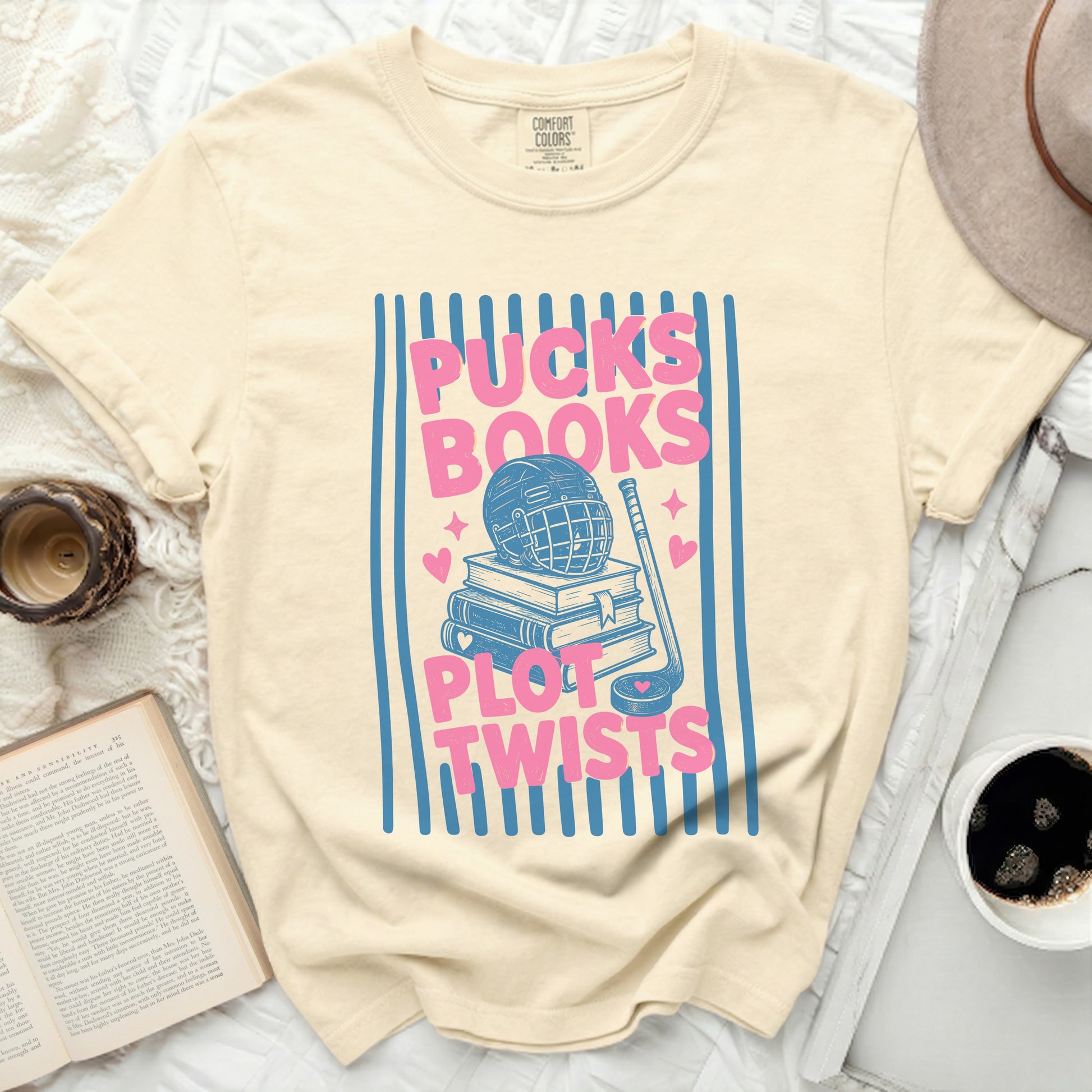 Cream t-shirt with "Pucks Books Plot Twists" graphic featuring hockey gear and books.