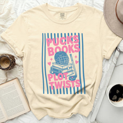Cream t-shirt with "Pucks Books Plot Twists" graphic featuring hockey gear and books.