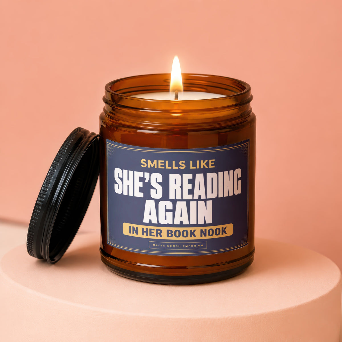 Brown jar candle with lit wick, "She's Reading Again" text on label.