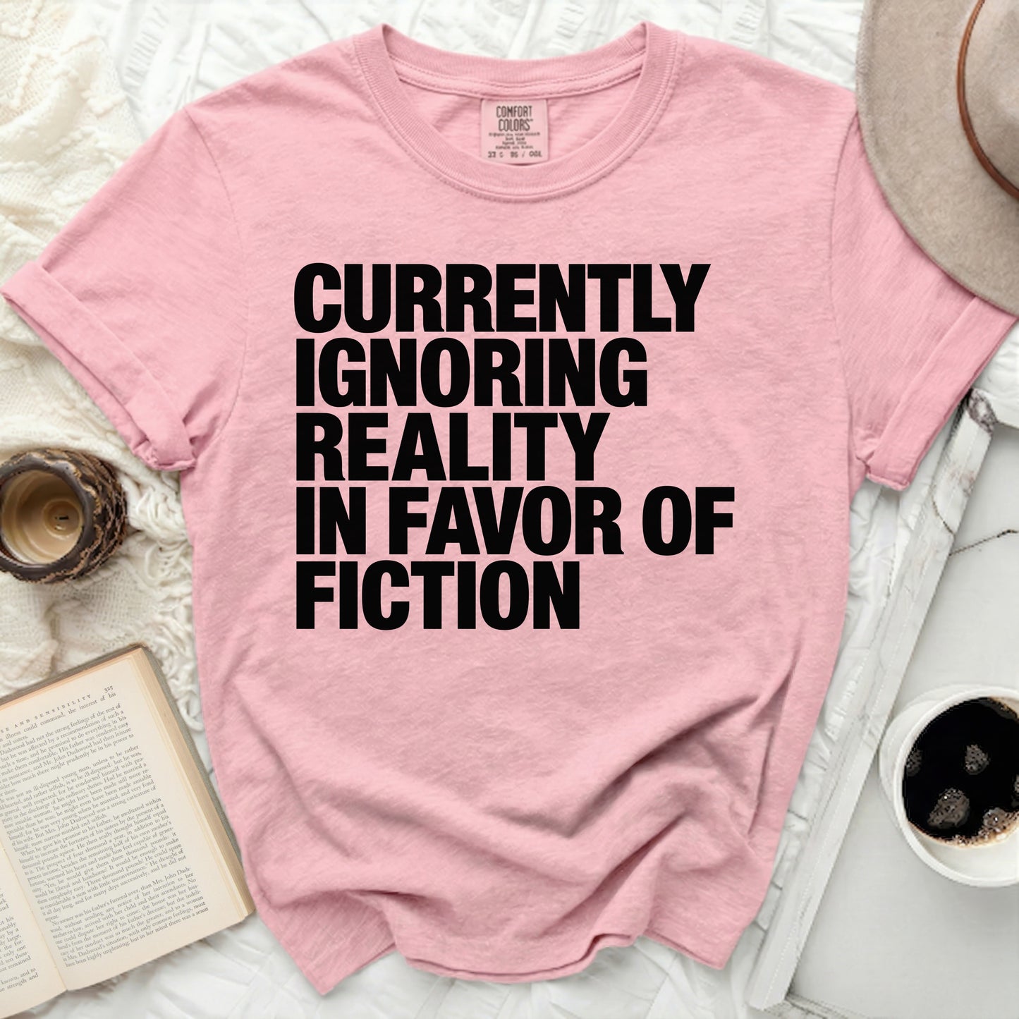 Pink t-shirt with black text: "Currently Ignoring Reality In Favor Of Fiction".