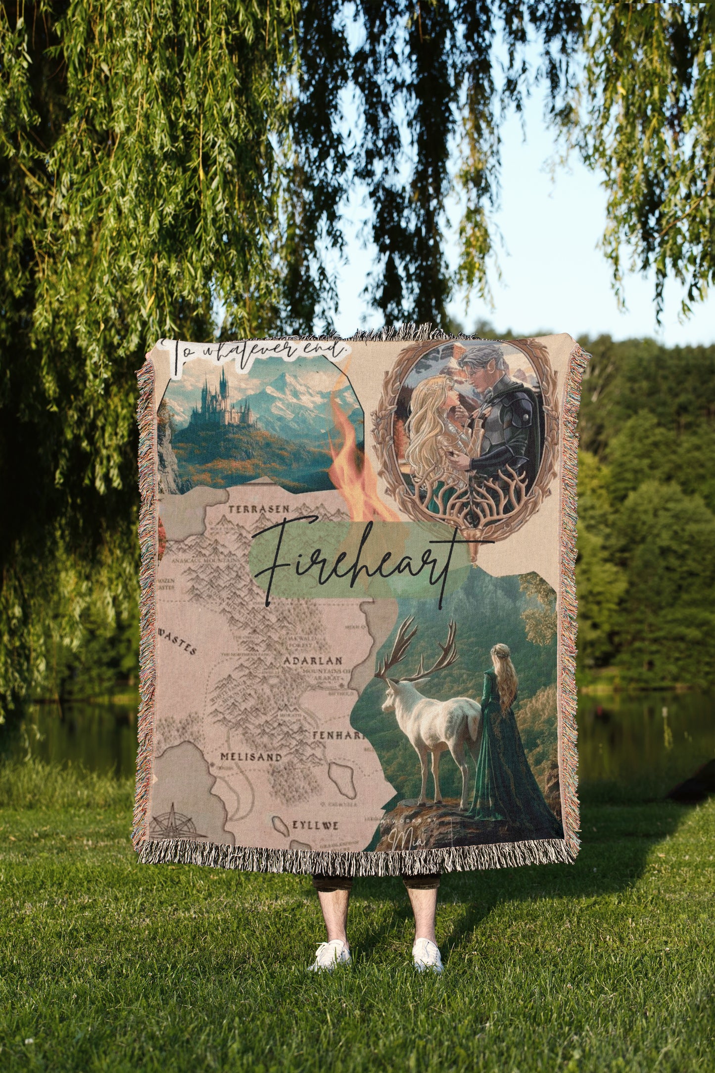 A person is standing in a grassy area, holding a large blanket that features a collage of images, including a map, a castle, a woman in a green dress, and a deer.