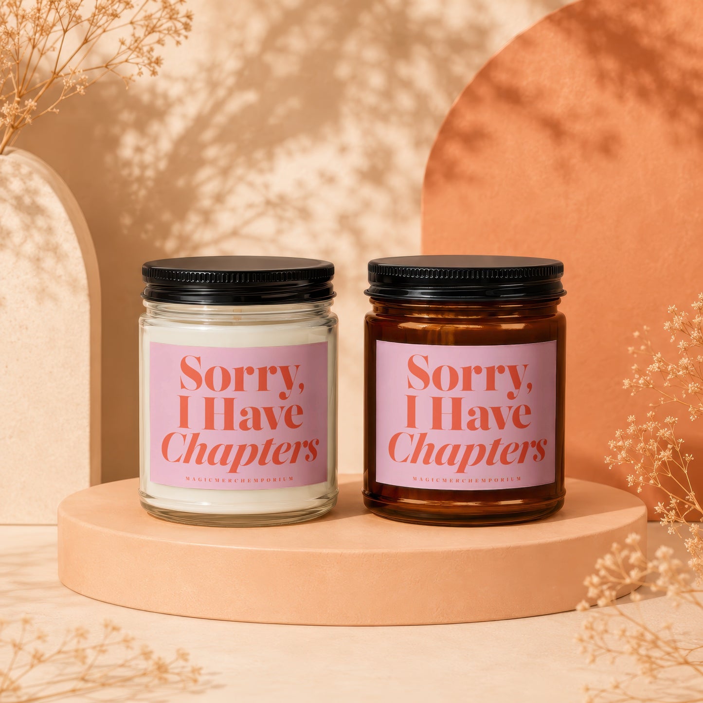 Two candles with "Sorry, I Have Chapters" on pink labels sit on a peach display.