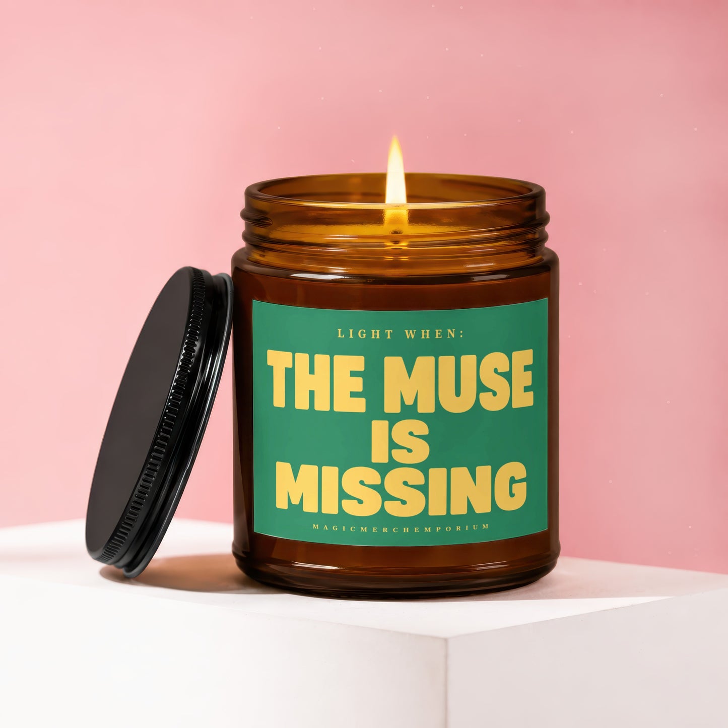 Amber glass candle with lit flame, green label reads "LIGHT WHEN: THE MUSE IS MISSING".