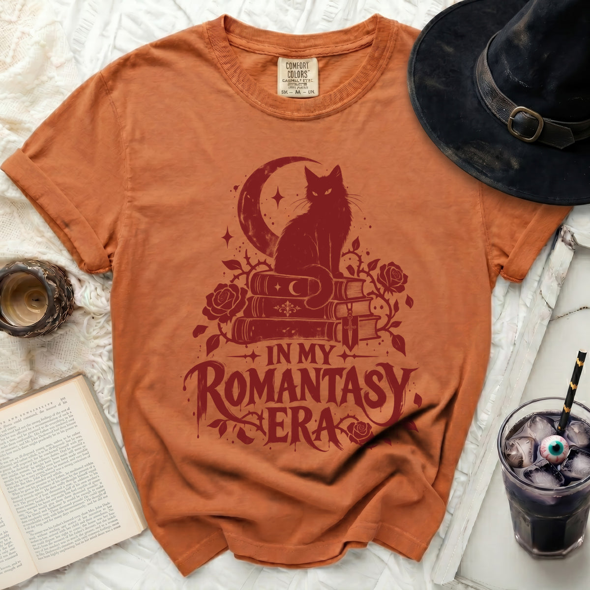 Orange t-shirt with red graphic of a black cat on books and moon.
