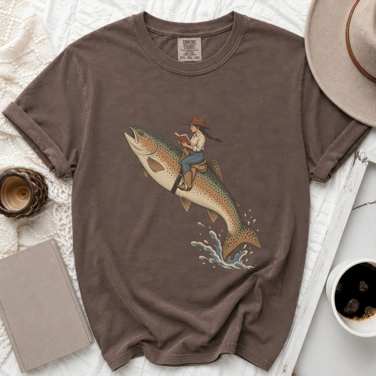 T-shirt with graphic of woman in cowboy hat riding a rainbow trout, reading.