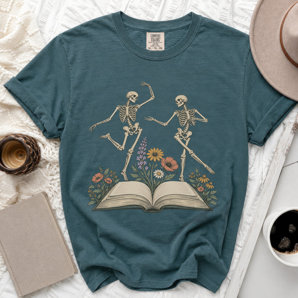 Teal t-shirt with dancing skeletons, an open book, and flowers design.