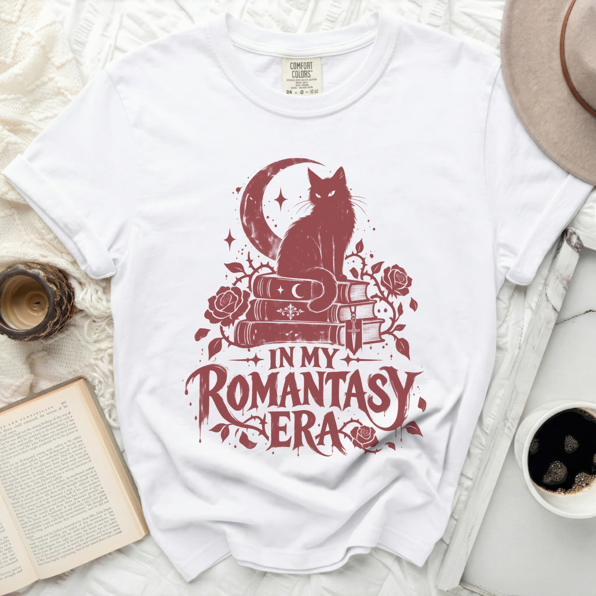 White t-shirt with a dark red graphic of a cat on books, moon, and roses. Text reads "In My Romantasy Era".
