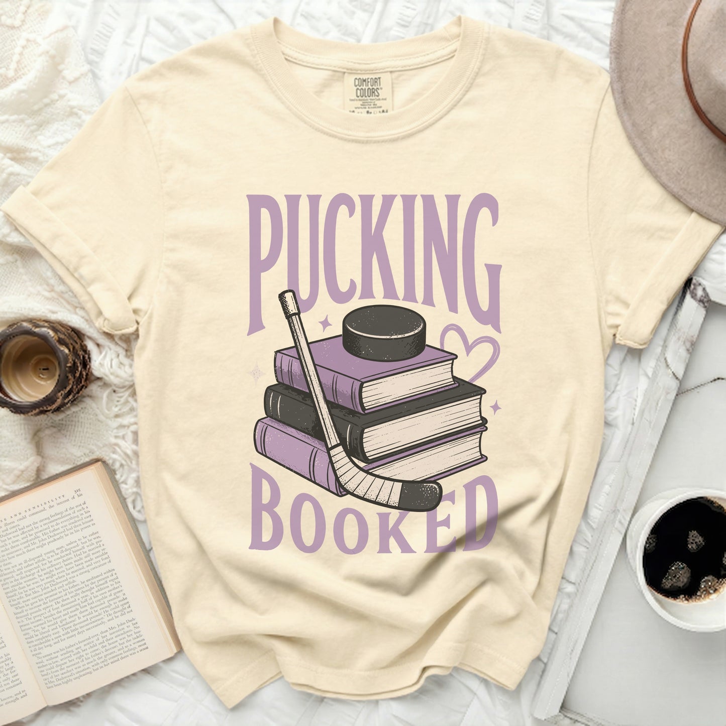 T-shirt with stacked books, hockey stick, and puck, saying "Pucking Booked".