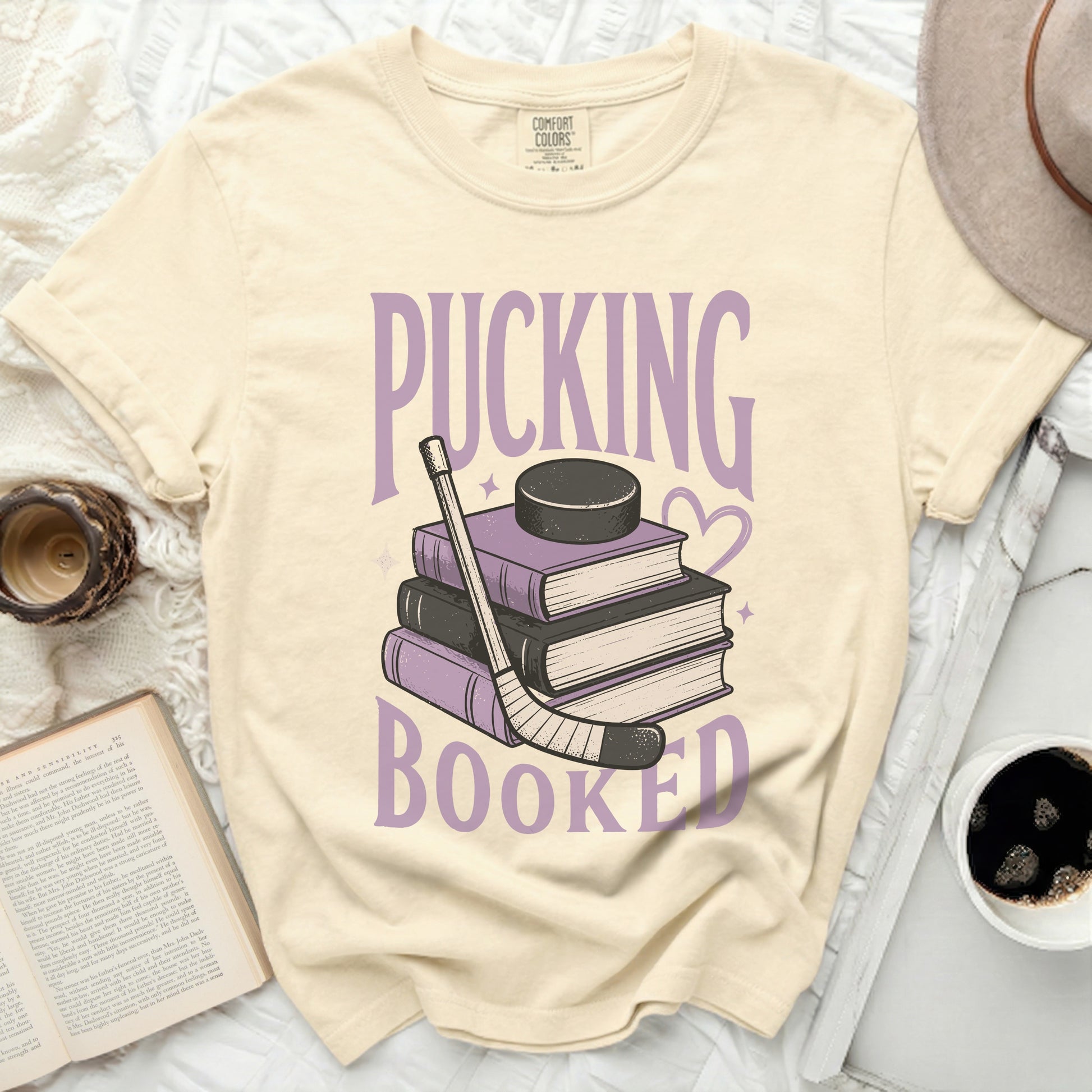 T-shirt with stacked books, hockey stick, and puck, saying "Pucking Booked".