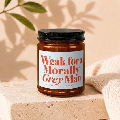 Candle with orange text "Weak for a Morally Grey Man" on a light blue label.