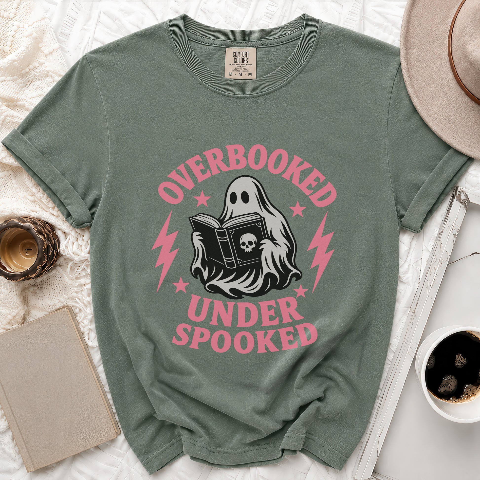 Ghost reading a book with text "overbooked under spooked" on green t-shirt.