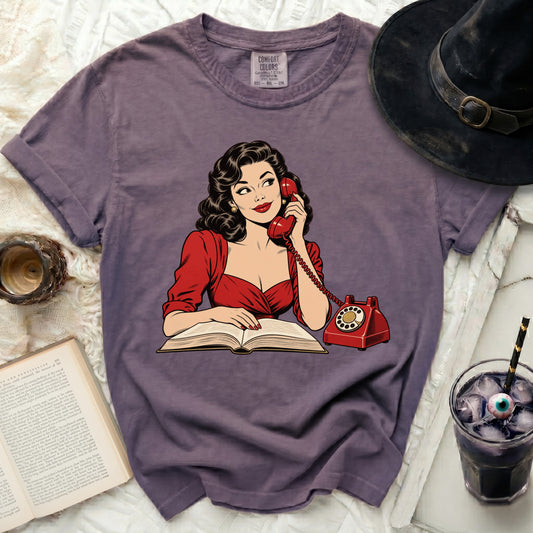 Purple t-shirt with retro comic graphic of woman on phone with open book.