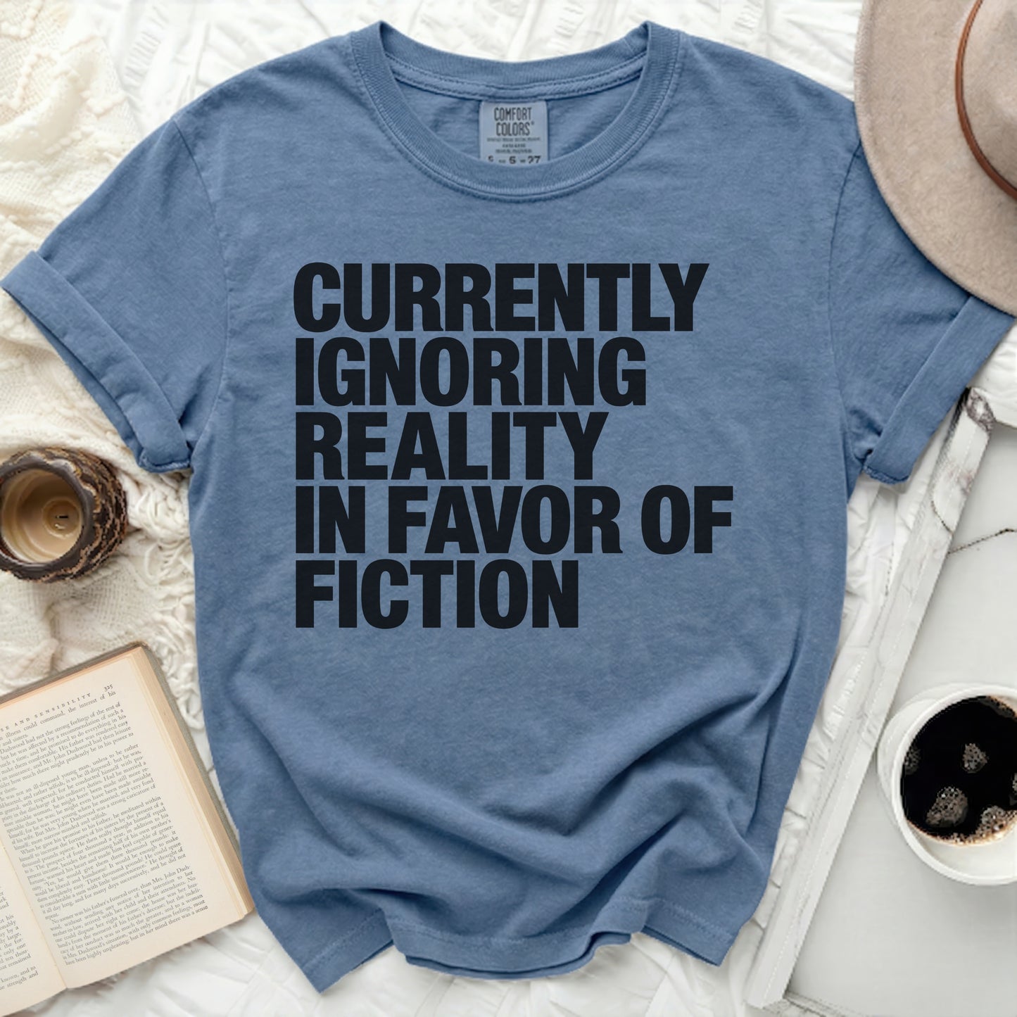 Blue t-shirt with "Currently Ignoring Reality In Favor Of Fiction" text.