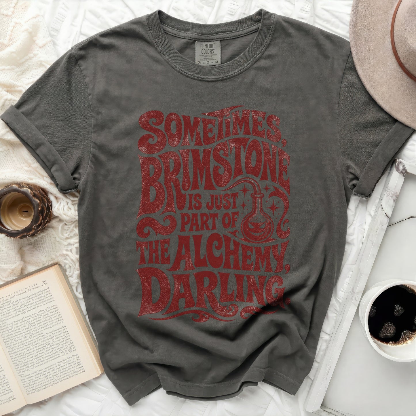 Dark gray t-shirt with "Sometimes Brimstone Is Just Part Of The Alchemy Darling" text.