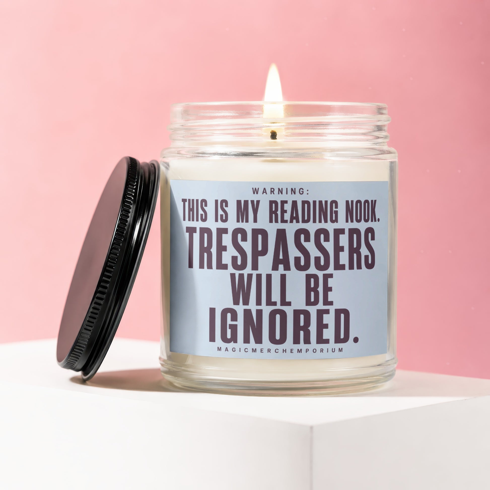 Glass candle with lit wick and black lid featuring text "WARNING: THIS IS MY READING NOOK. TRESPASSERS WILL BE IGNORED."