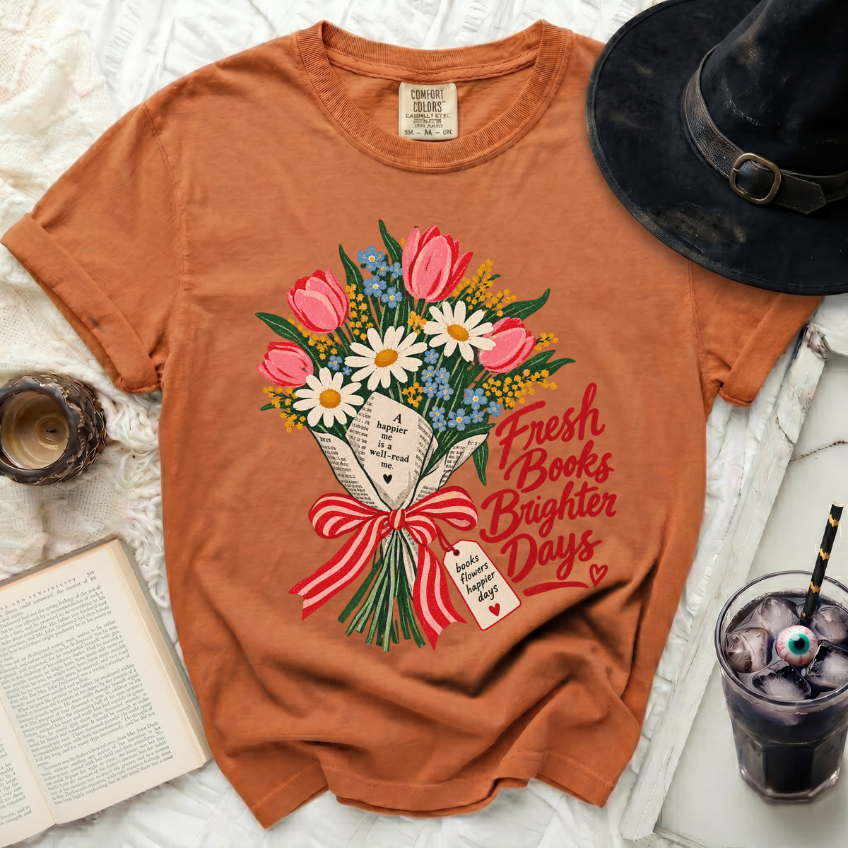 Orange t-shirt with a bouquet of flowers, books, and text "Fresh Books Brighter Days".