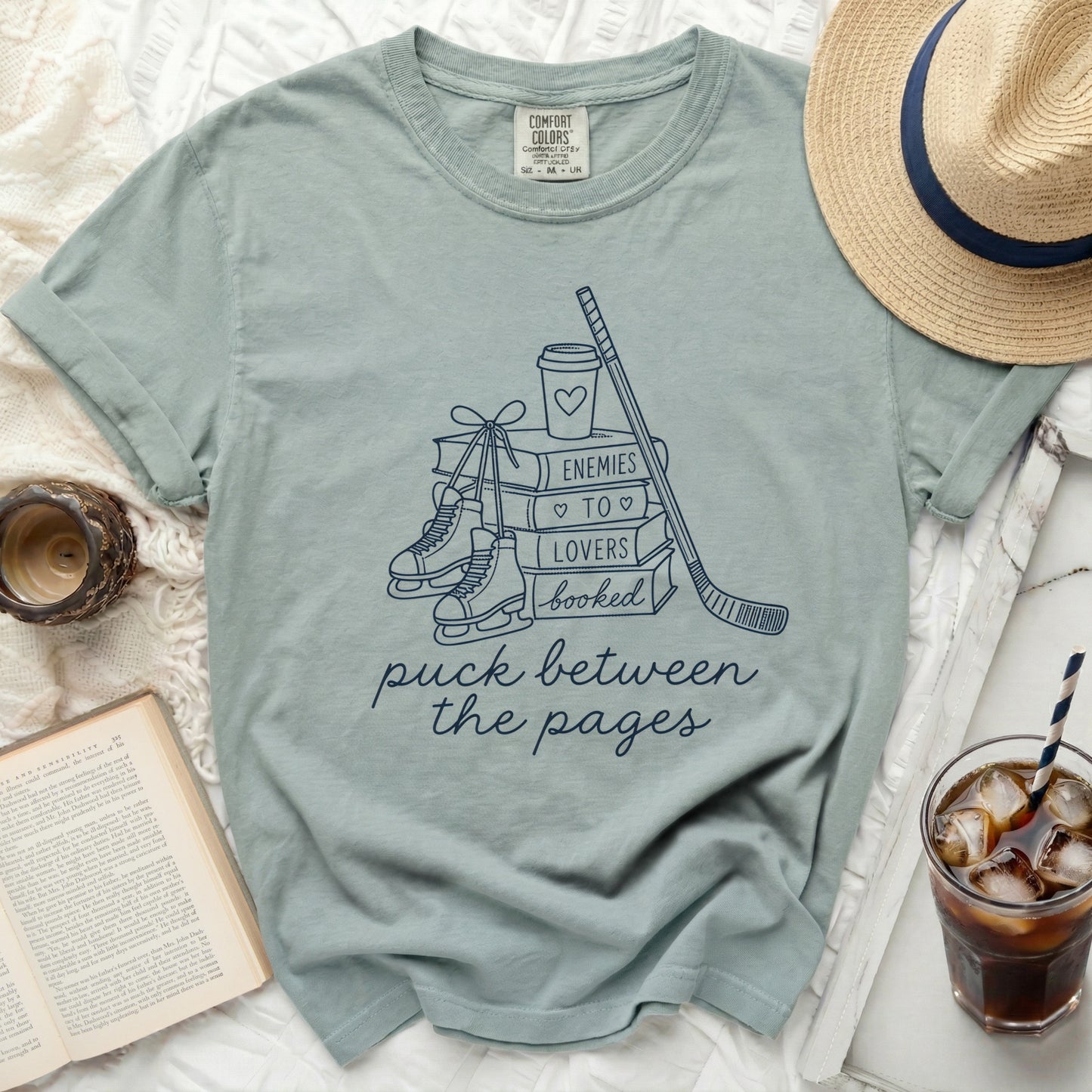 T-shirt with ice skates, hockey stick, and "enemies to lovers" book stack design.