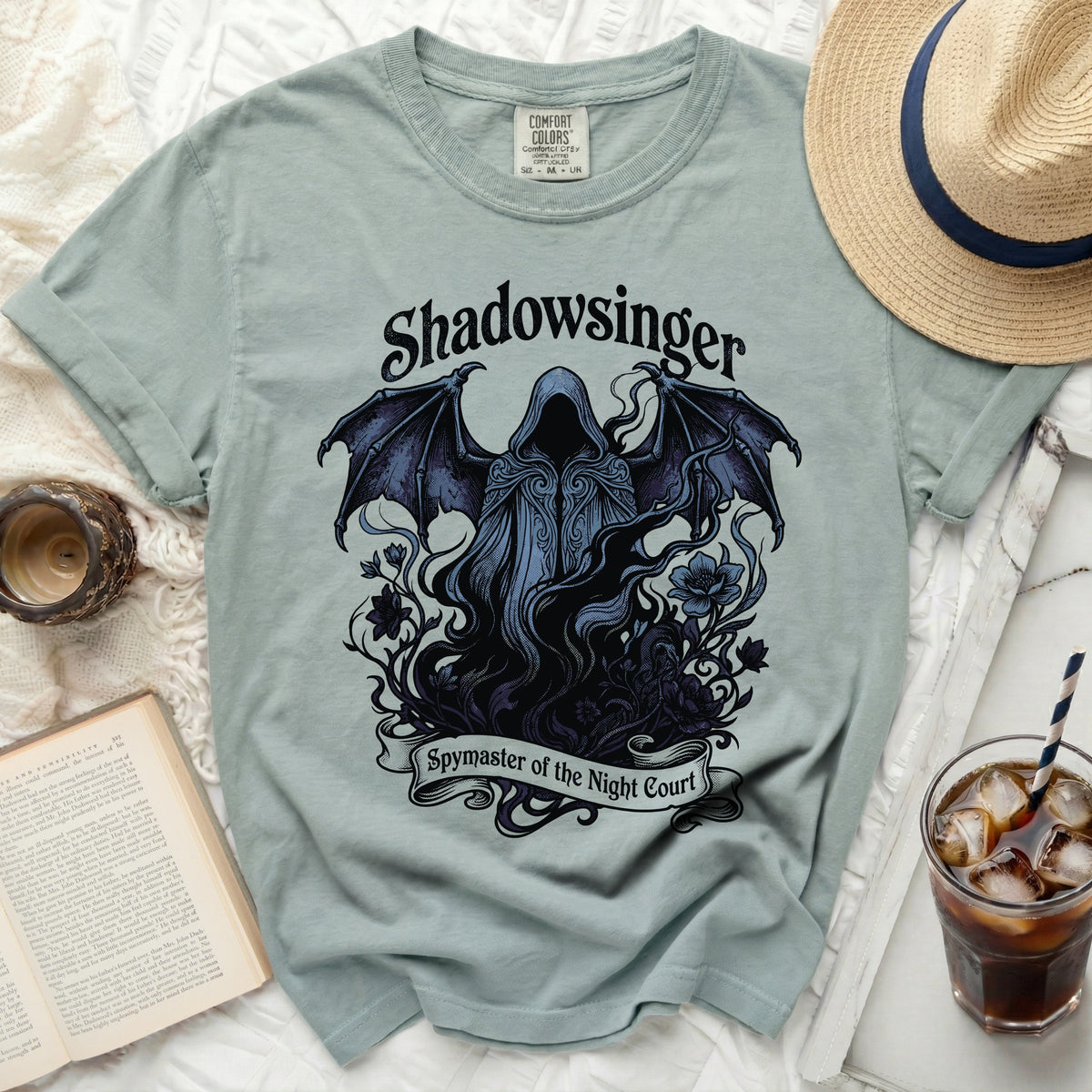 Light blue t-shirt with a dark graphic of a hooded figure with wings, text "Shadowsinger Spymaster of the Night Court".