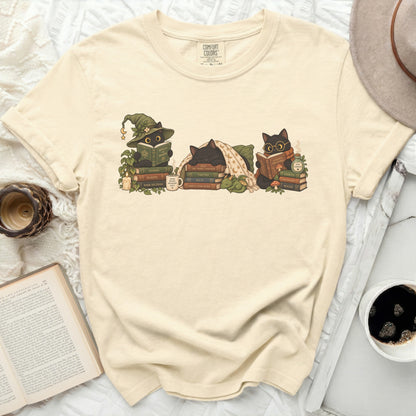 Cream t-shirt with three black cats reading books and a dragon figurine.