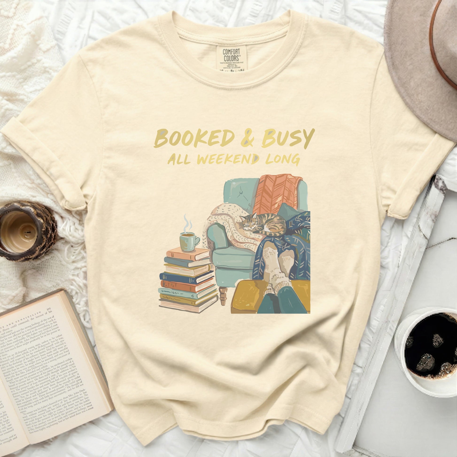 T-shirt with "Booked & Busy All Weekend Long" graphic and book, cat, and coffee motif.