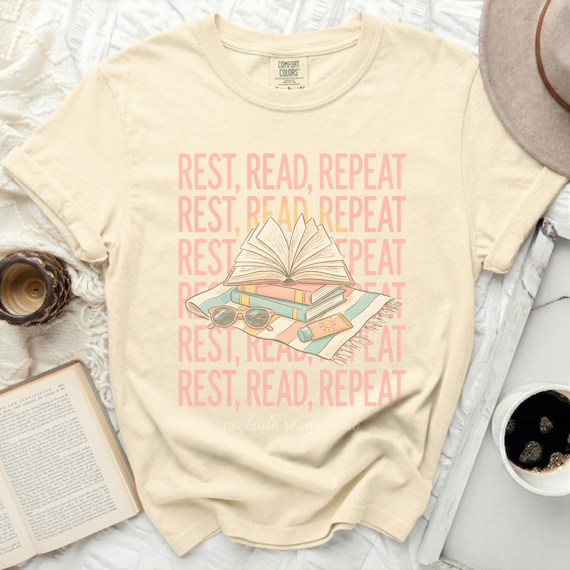 Cream t-shirt with "REST, READ, REPEAT" repeating text and book graphic.