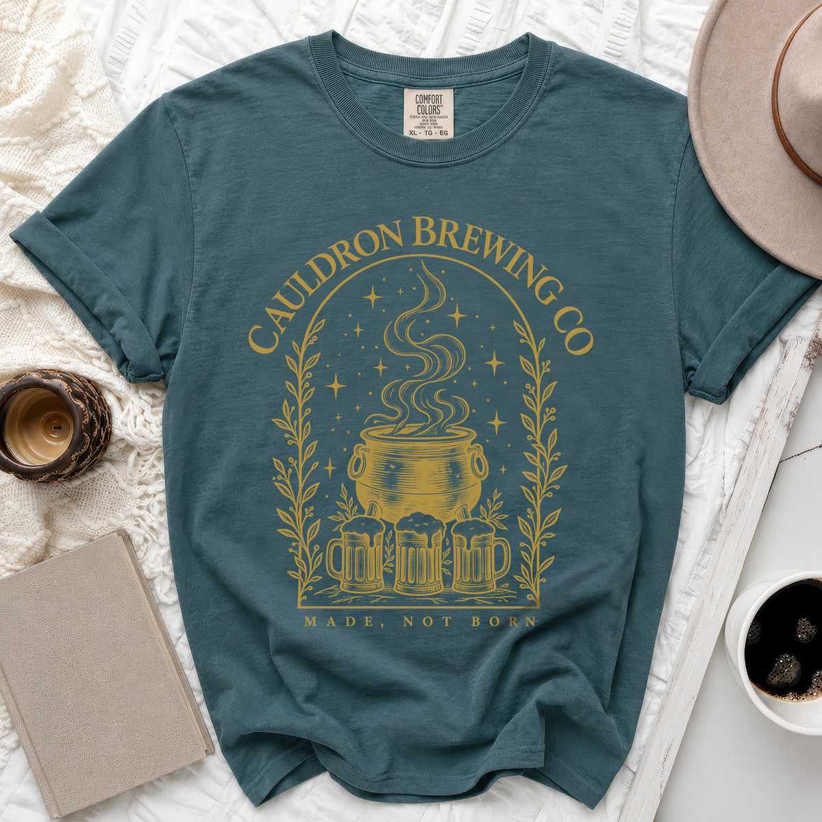 Slate blue crewneck t-shirt featuring a gold graphic of a steaming cauldron, beer mugs, and stars.