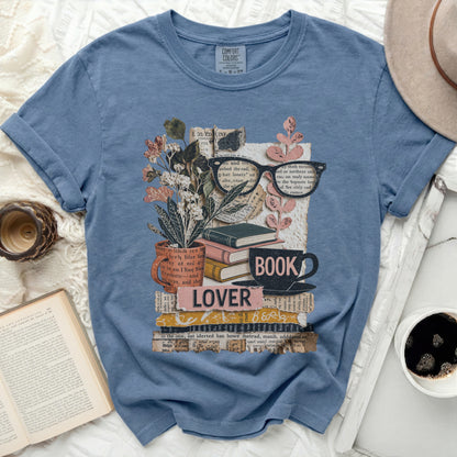 Blue t-shirt with a collage of books, glasses, flowers, and the word "LOVER".