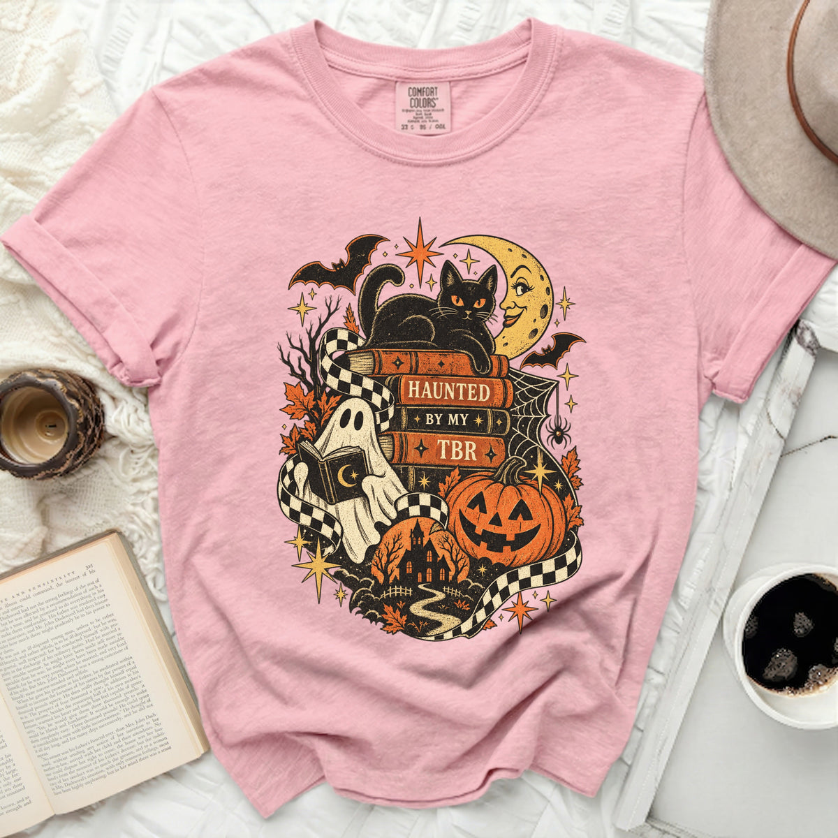 Pink t-shirt with Halloween graphic: black cat on books reading "HAUNTED BY MY TBR".
