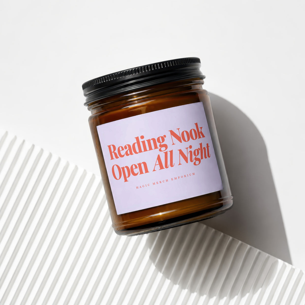 Amber glass candle with a black lid and a lavender label reading "Reading Nook Open All Night".