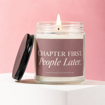 Glass candle with lit wick, black lid, and label that reads "Chapter First. People Later. MAGICMERCHTEMPORIUM."