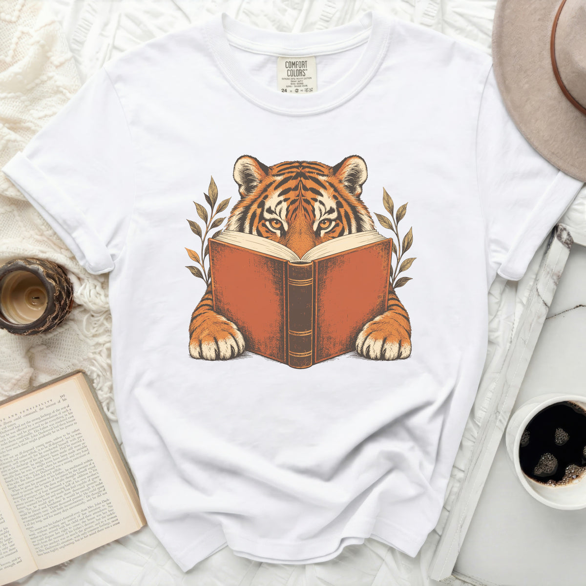 White t-shirt featuring a tiger reading a book, surrounded by leaves.